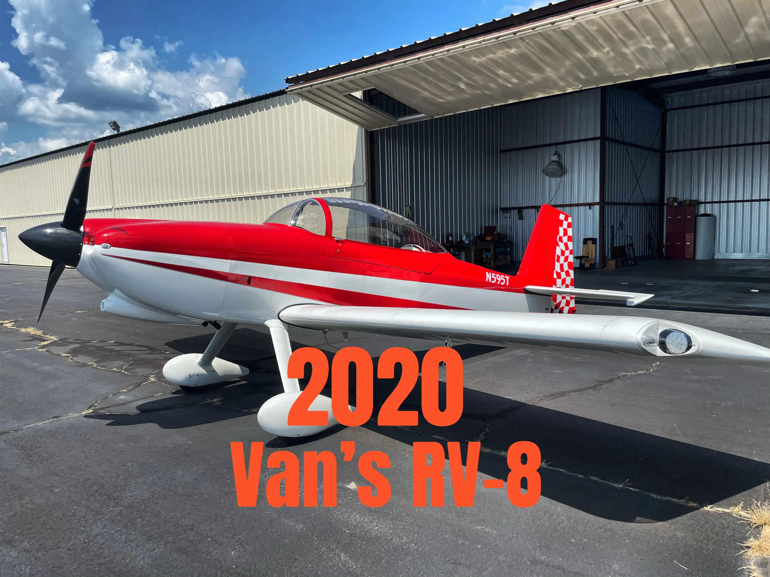 A red and white Van's RV-8 aircraft with a checkered tail sits on an asphalt tarmac in front of an open hangar.