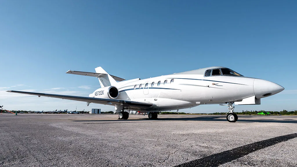 A white business jet with blue and grey stripes, tail number N9793K, parked on an airfield under a clear sky.
