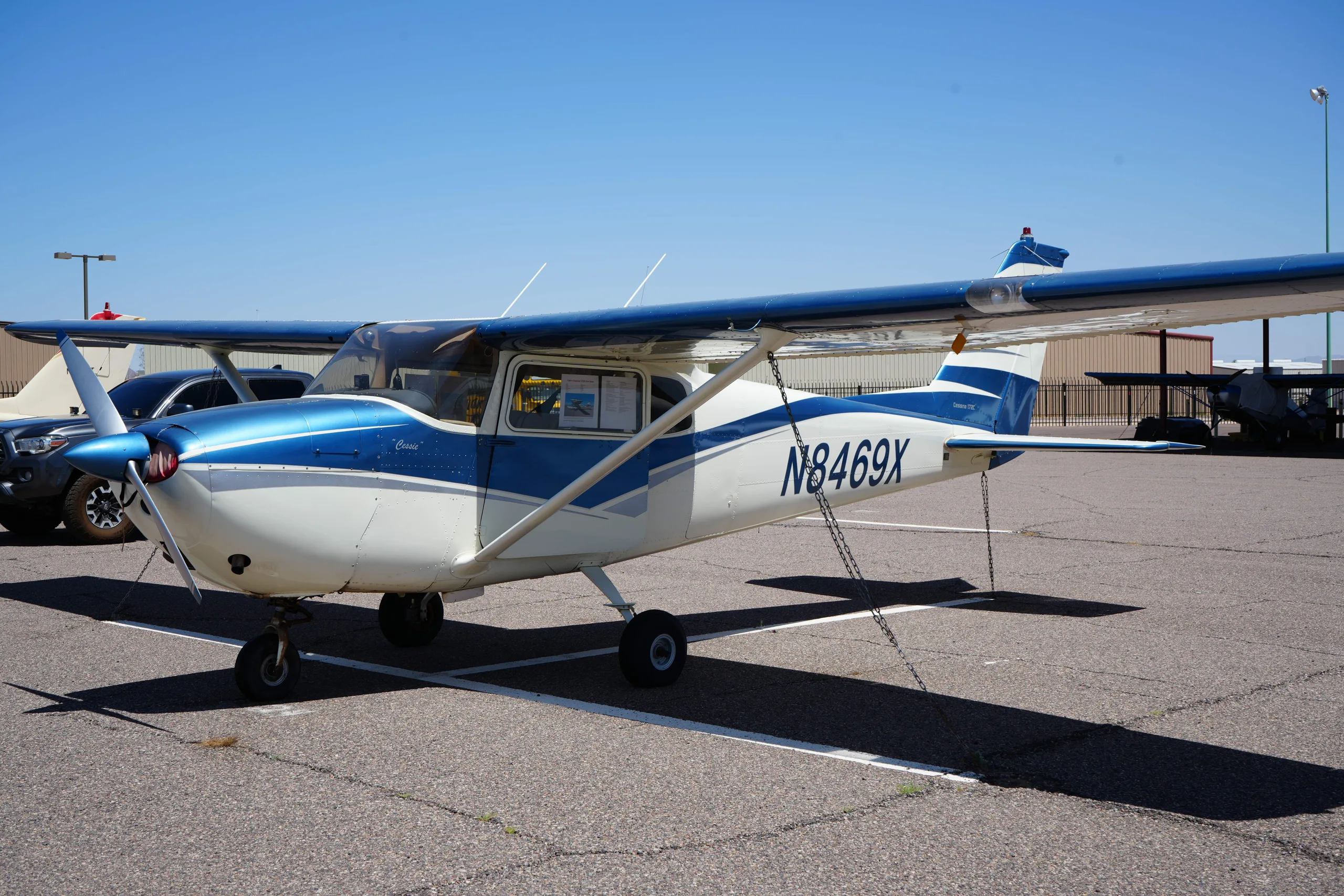 Close-up side view of a white and blue Cessna 172 (N8469X) on an airfield, showing the registration number.