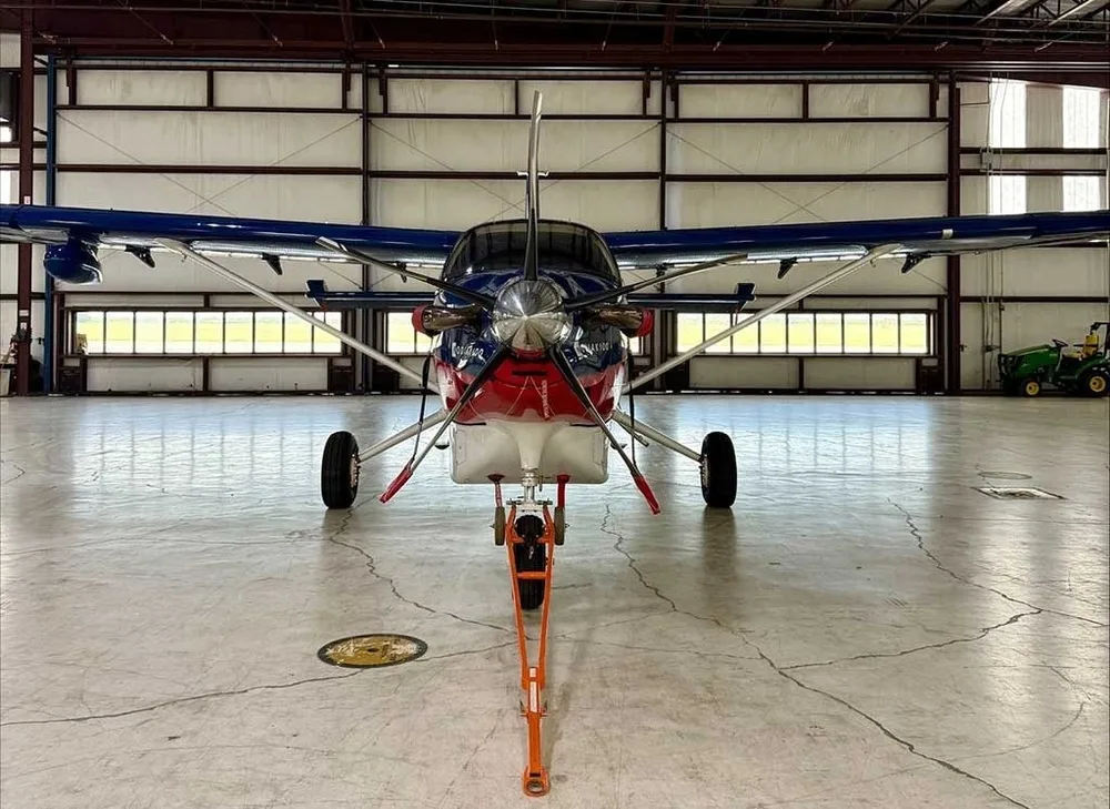 Front view of a Kodiak 100 aircraft with a blue, red, and white paint scheme, parked in a hangar.