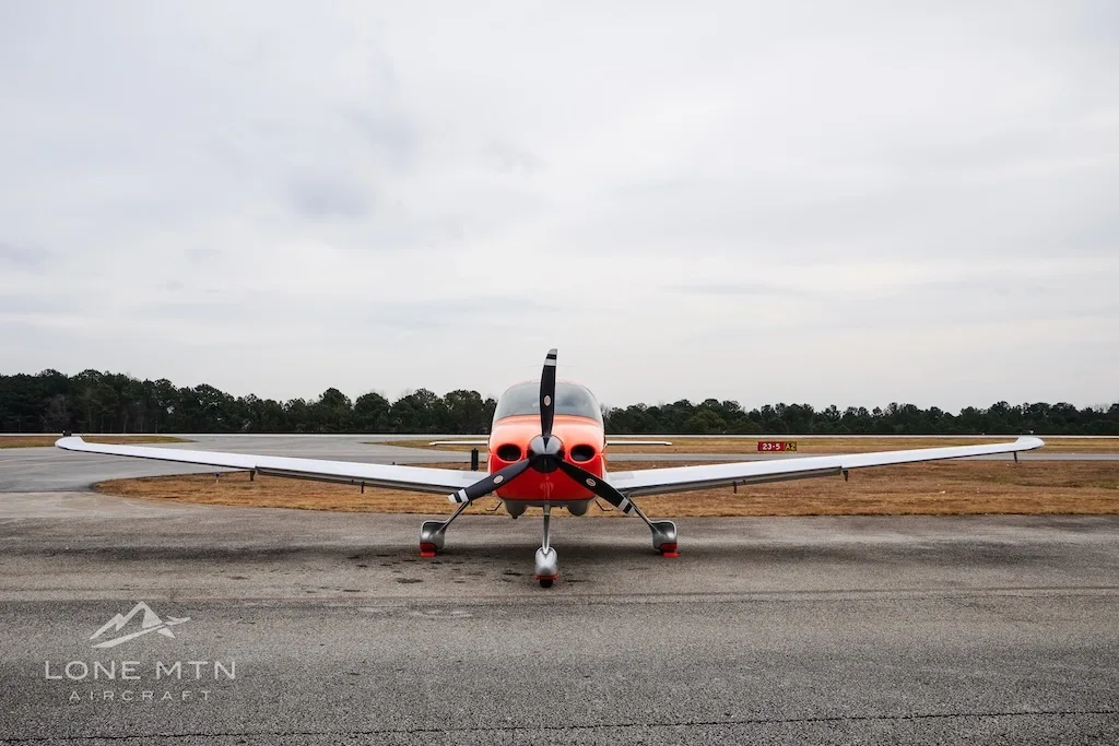 A head-on view of the orange and silver Cirrus SR20 aircraft N685MB on an airfield.