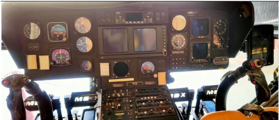 The cockpit of a helicopter showing the instrument panel with various gauges, screens, and flight controls.