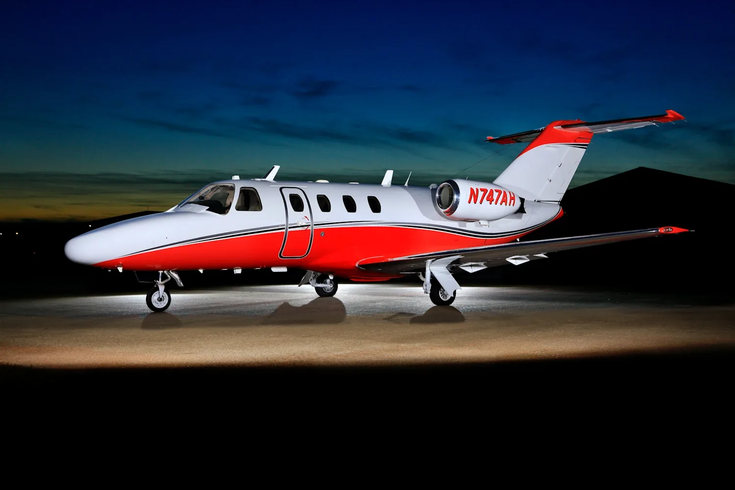 A white and red business jet, registration N747AH, is parked on a tarmac at twilight.
