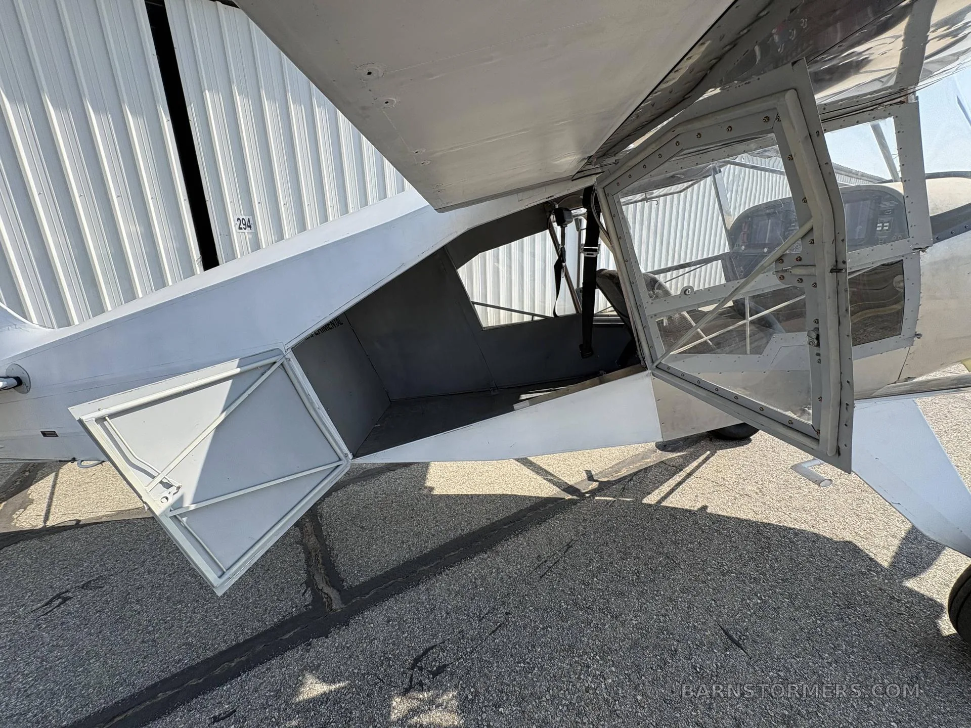 The open side door and cargo compartment of a silver and white aircraft, showing the interior space and a seatbelt.