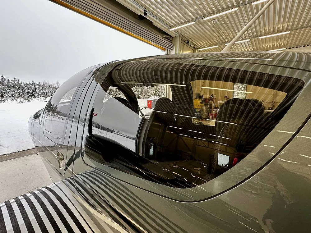 A close-up view of the cockpit and cabin windows of a gray Diamond DA62 aircraft, showing the interior and a snowy landscape outside.