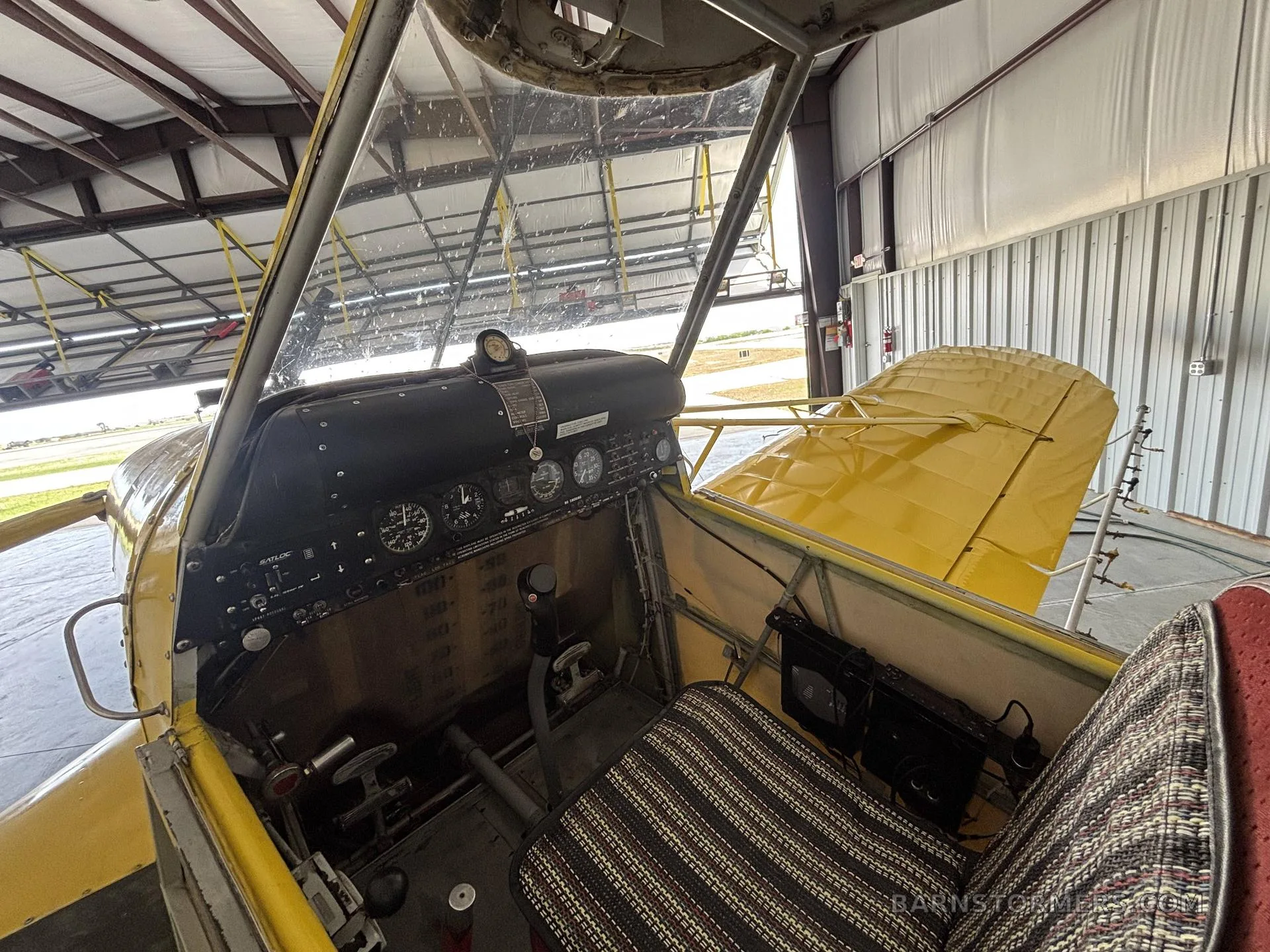 View from inside the cockpit of a yellow Piper PA-25 Pawnee, showing the instrument panel and a striped seat.