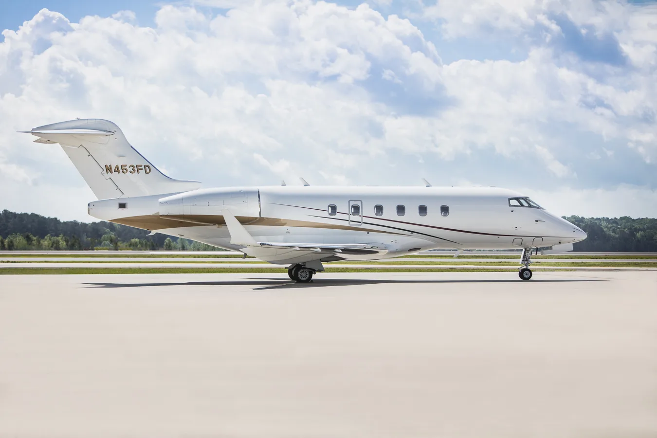 Full side view of a white business jet with N453FD registration, featuring gold and maroon stripes, on an airfield.
