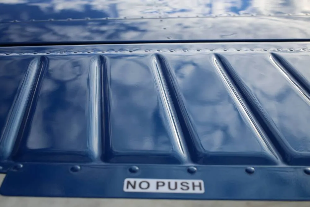 A close-up view of a shiny blue aircraft surface with "NO PUSH" text, reflecting the sky.