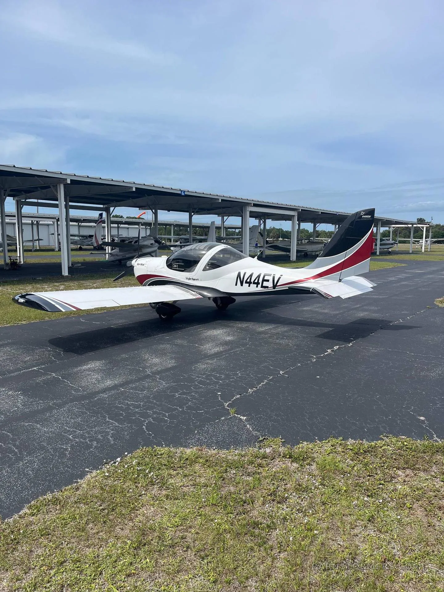 A white and red SportStar aircraft, tail number N44EV, parked on an asphalt ramp with hangars in the background.