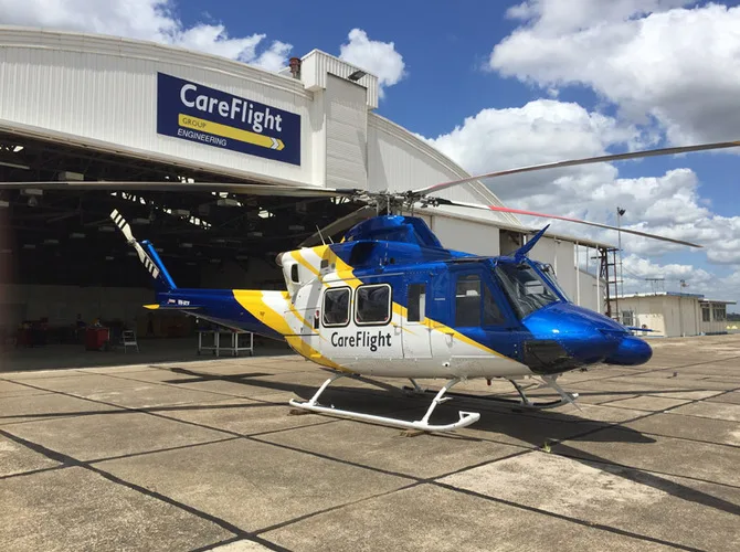 A blue, white, and yellow CareFlight helicopter, likely a Bell 412, parked on a tarmac in front of a hangar under a partly cloudy sky.