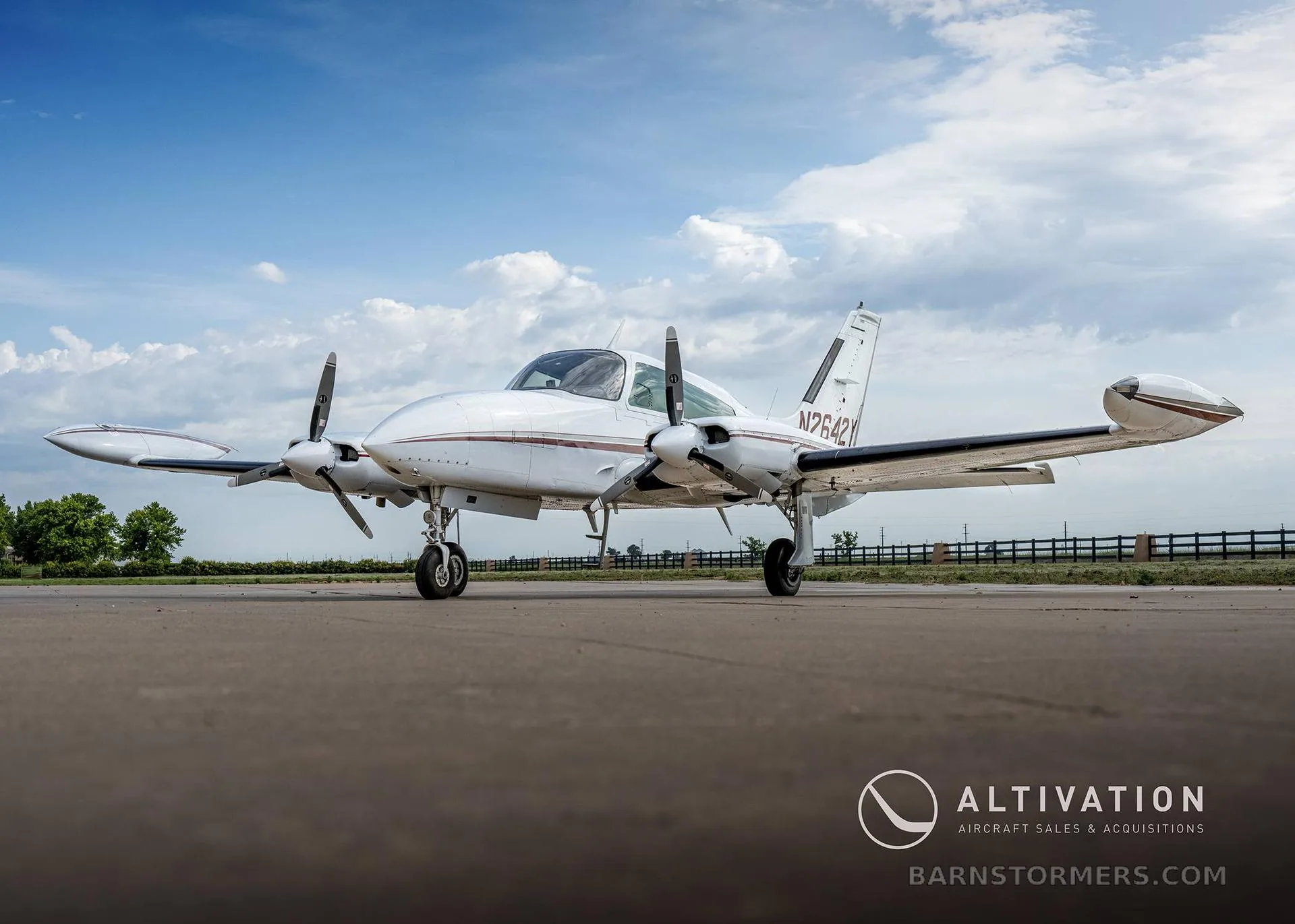 A low-angle front-side view of a white twin-engine propeller aircraft with maroon stripes, registration N2642Y, parked on an asphalt runway.