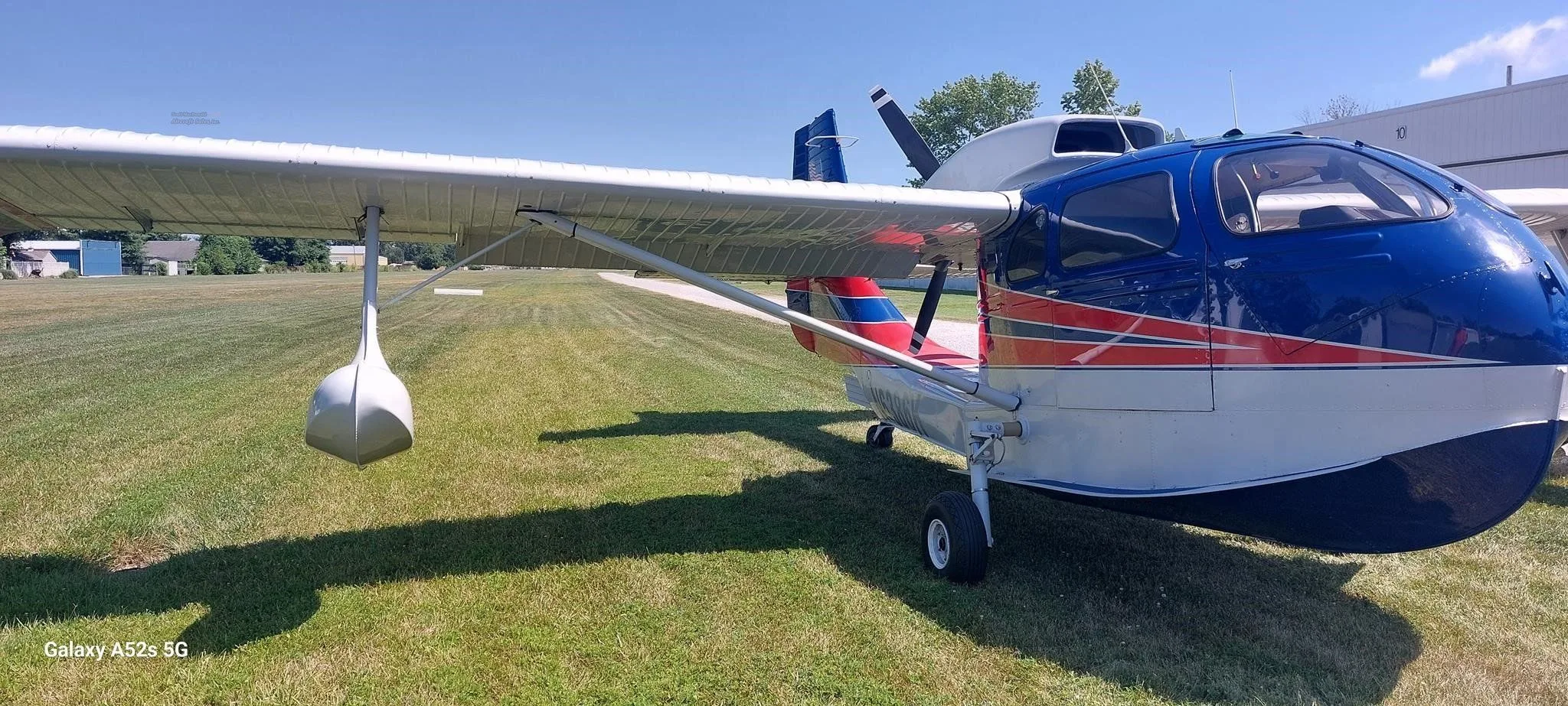 A blue, white, and red amphibious aircraft with registration N6386K parked on a grassy field.