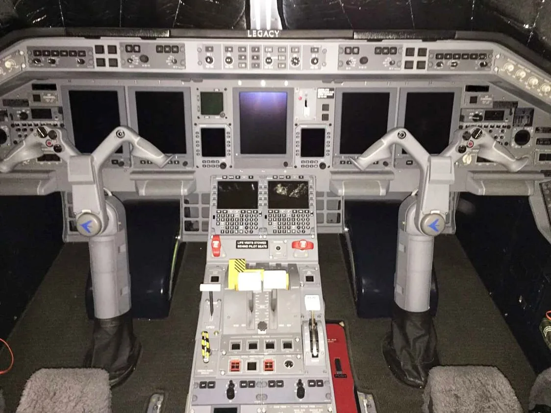 The modern cockpit of a Legacy aircraft, featuring multiple digital displays and a complex control panel.