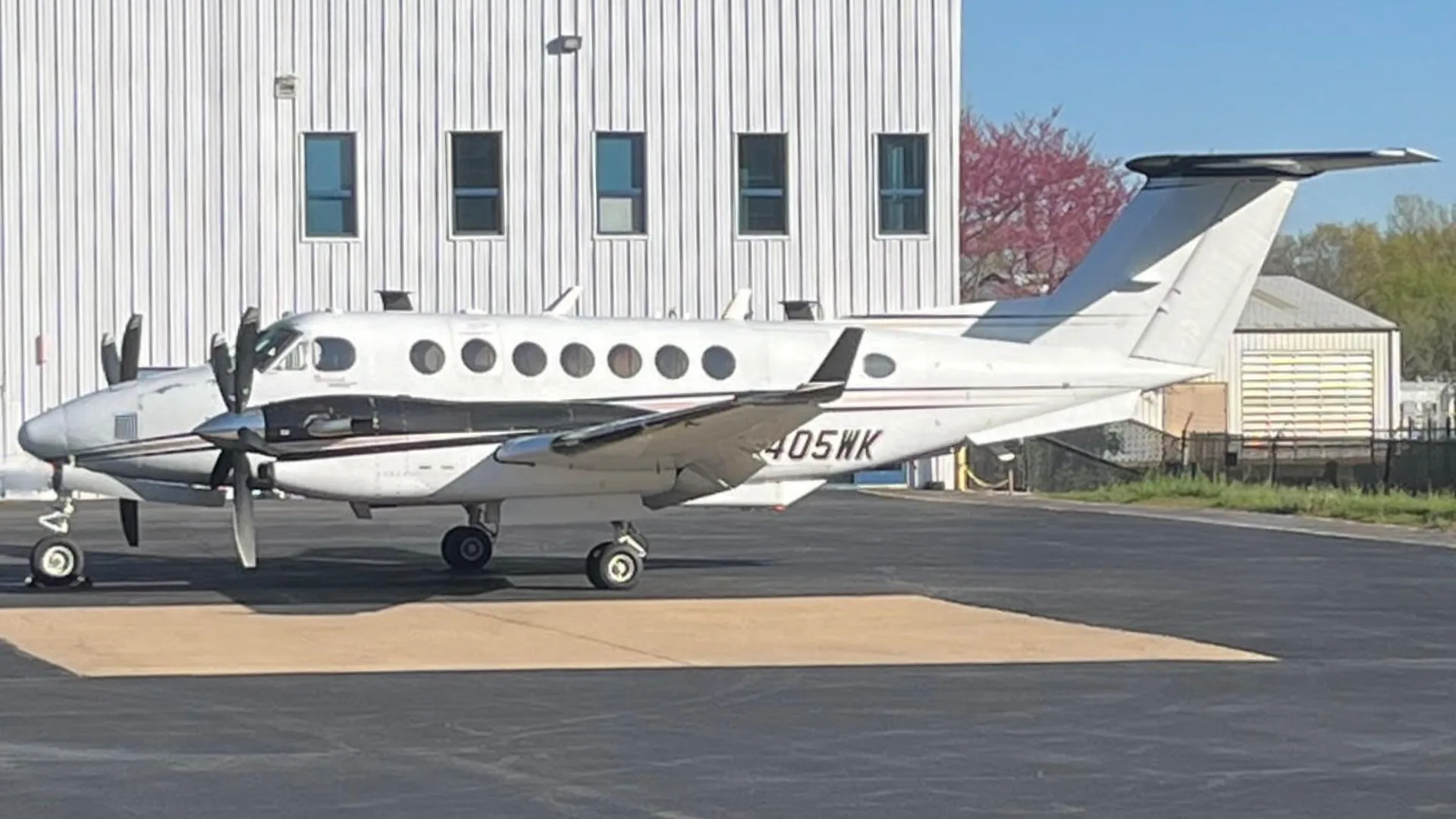 A white and black Beechcraft King Air N405WK parked on an asphalt tarmac next to a white building.