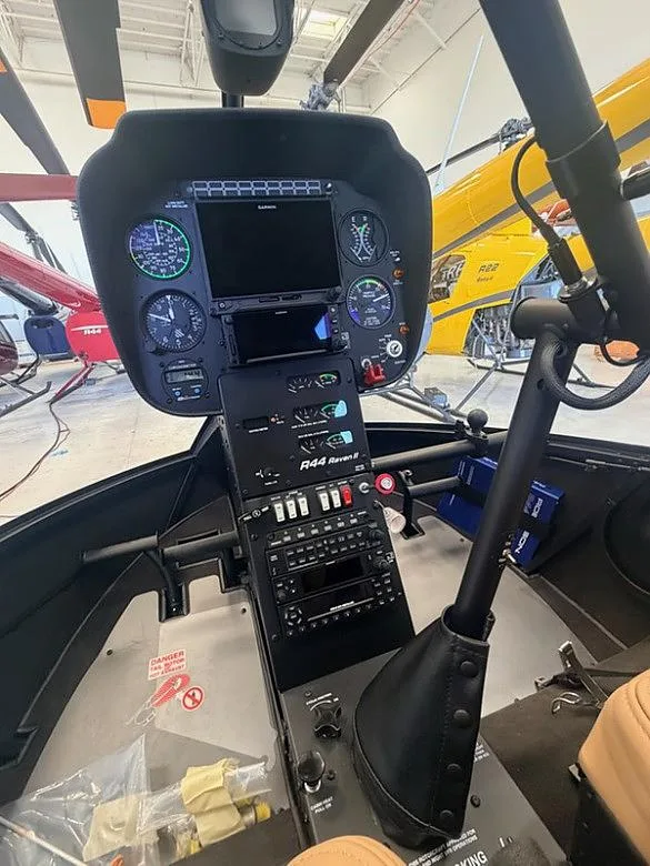 The cockpit of a Robinson R44 Raven II helicopter, showing the instrument panel, cyclic, and collective controls.