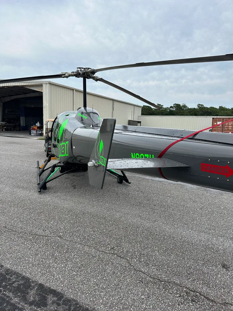 A rear view of the gray Enstrom helicopter N88ZH, showing its tail boom and rotor.