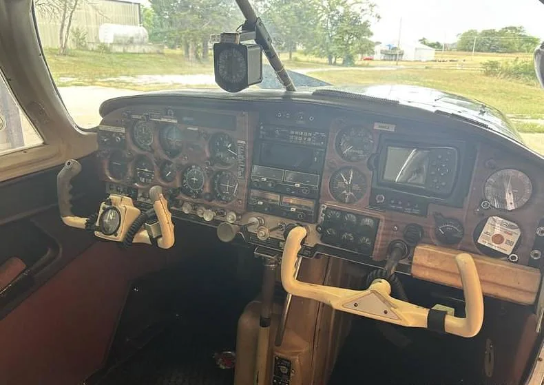 The cockpit of a Mooney M20 aircraft, showing the instrument panel with analog gauges and a modern display.