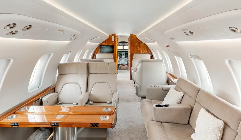 A spacious private jet cabin with a comfortable sofa, individual seats, and a large wooden table.
