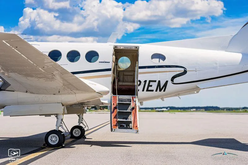 Close-up side view of a white twin-engine turboprop aircraft with its passenger door open, revealing the integrated airstairs.