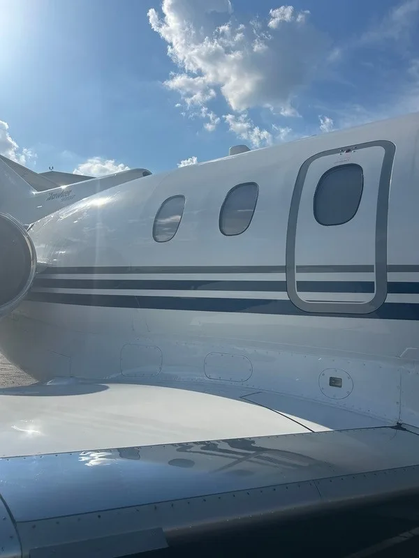 A close-up view of the passenger windows and entry door area on the white fuselage of a business jet, with part of the wing visible.