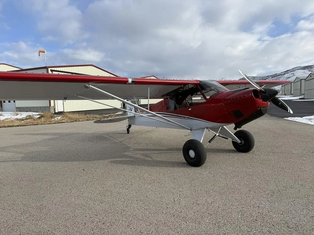 A red and white bush plane with large tires parked on an asphalt runway in front of hangars.
