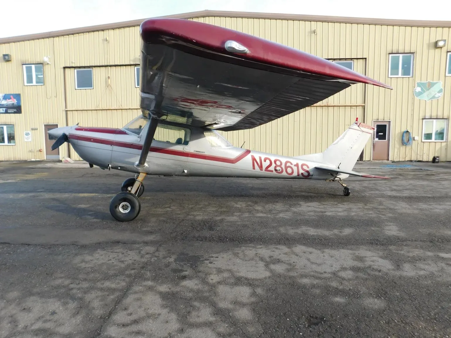 A silver and red single-engine propeller aircraft (N2861S) parked on a tarmac next to a hangar.