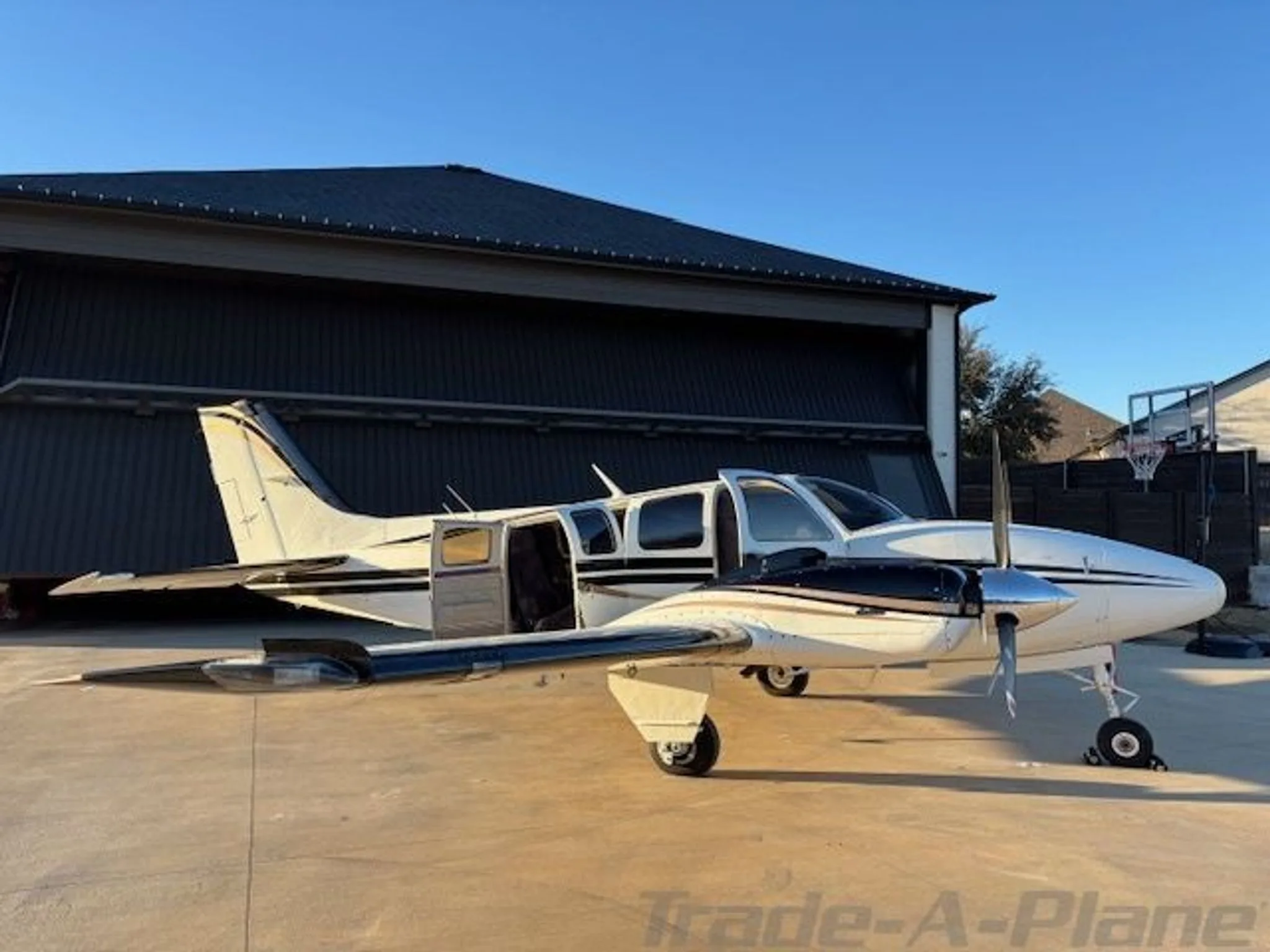 A white and black twin-engine aircraft with gold stripes and open passenger doors parked on a tarmac.