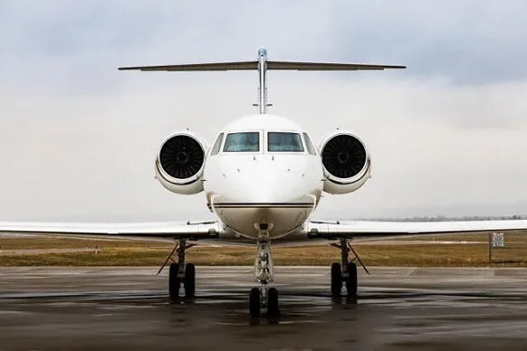 A front view of a white business jet parked on a wet tarmac under an overcast sky.