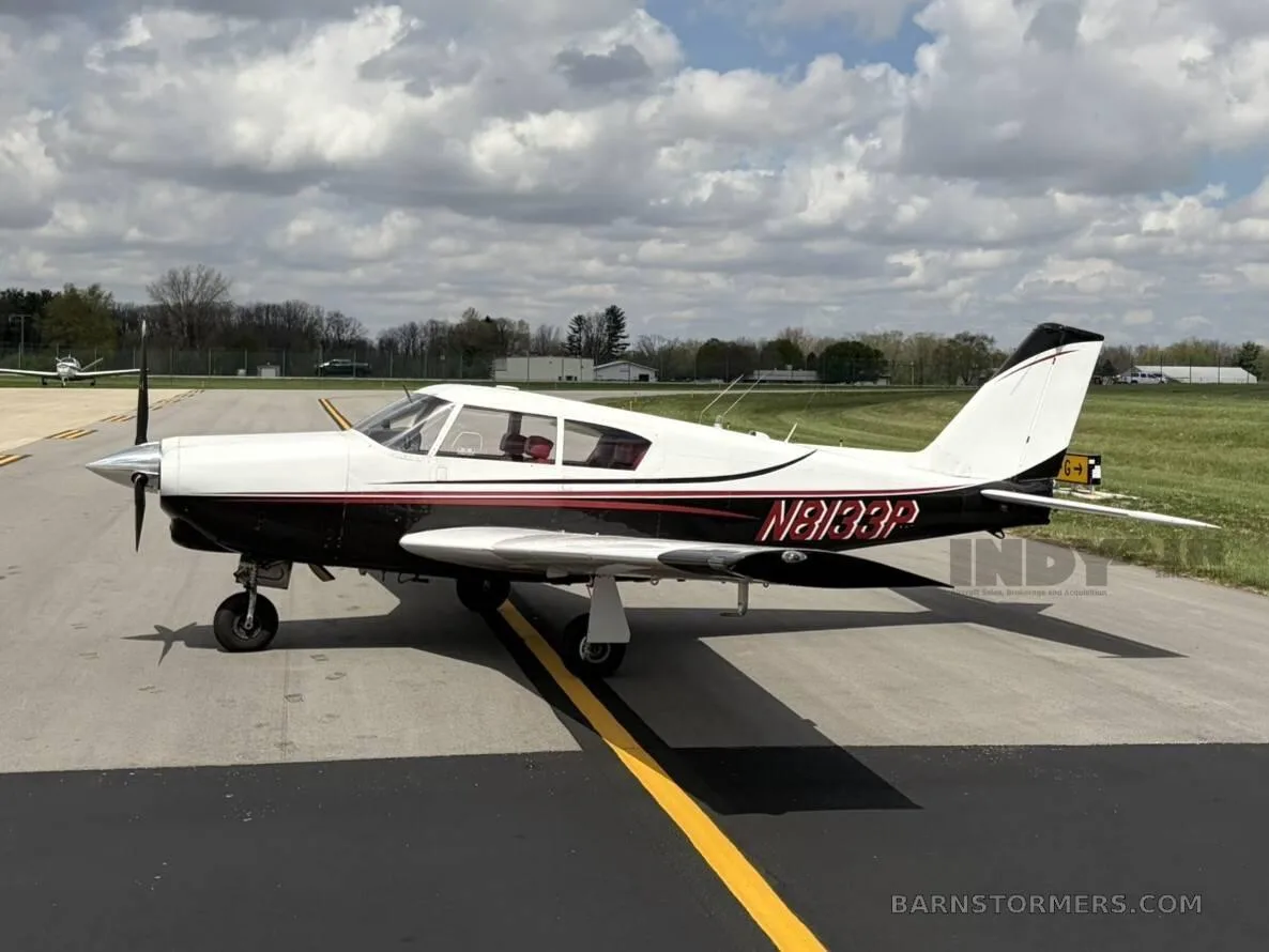 A white and black single-engine propeller aircraft with red accents, viewed from the left side, parked on an asphalt taxiway.