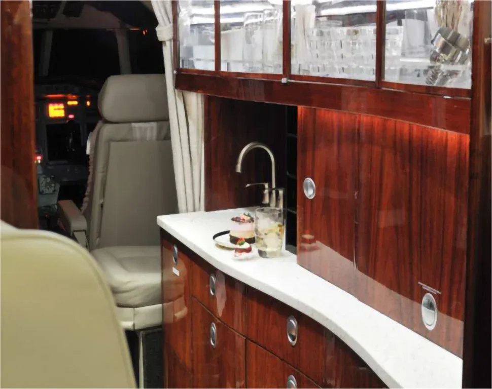 An aircraft galley with a white countertop, sink, and dark wood cabinets, with a view into the cockpit.