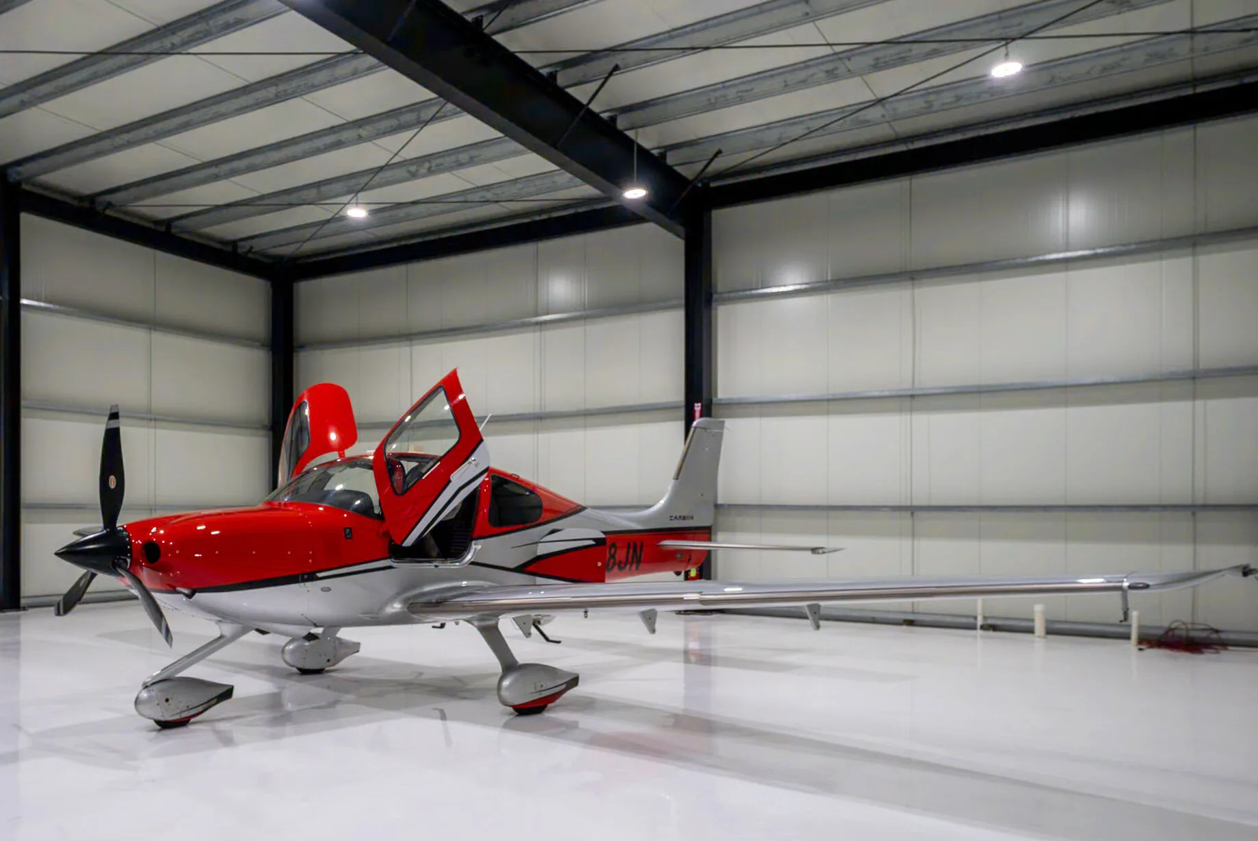 A red and silver Cirrus SR22T Carbon aircraft with registration N48JN and open doors, parked in a hangar.
