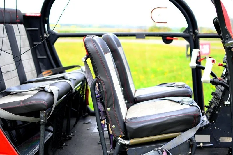 The interior of a helicopter showing black and white upholstered seats with red stitching, with a green field visible outside.