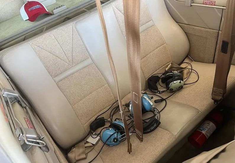 The tan rear cabin seats of a Beechcraft Bonanza with aviation headsets and a fire extinguisher.