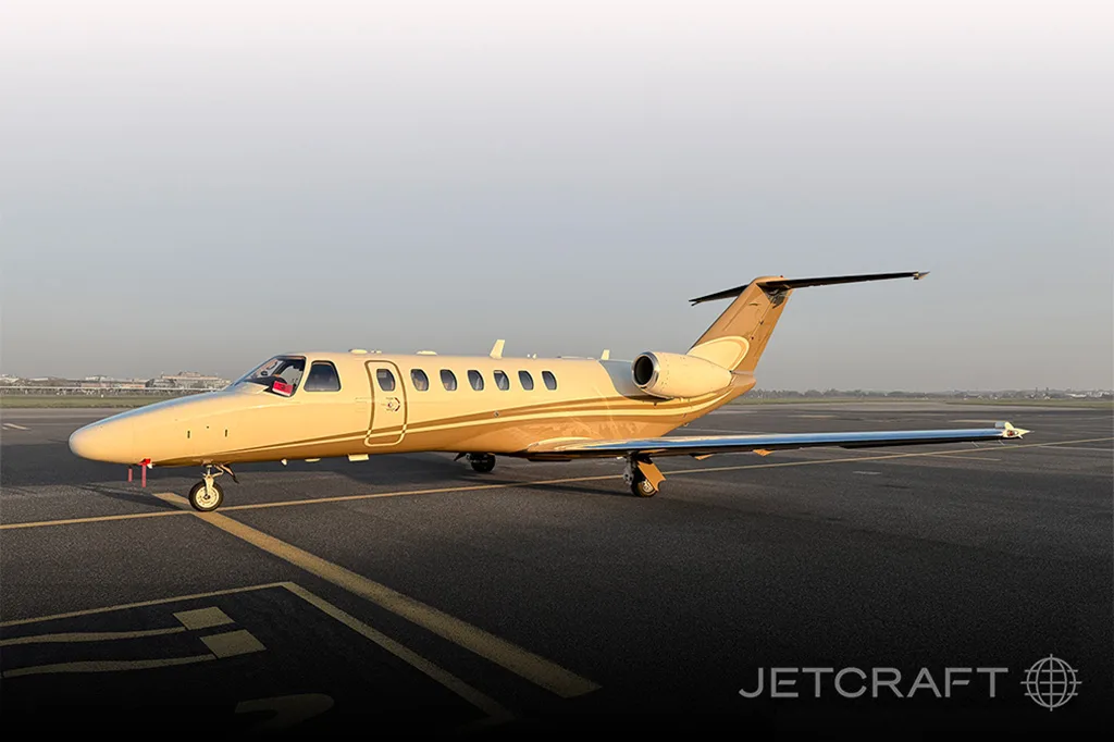 A Cessna Citation business jet with a gold and brown paint scheme is parked on an airfield under a clear sky.