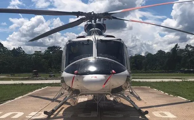A front view of a red, white, and black Bell 412 helicopter on a helipad under a cloudy sky.