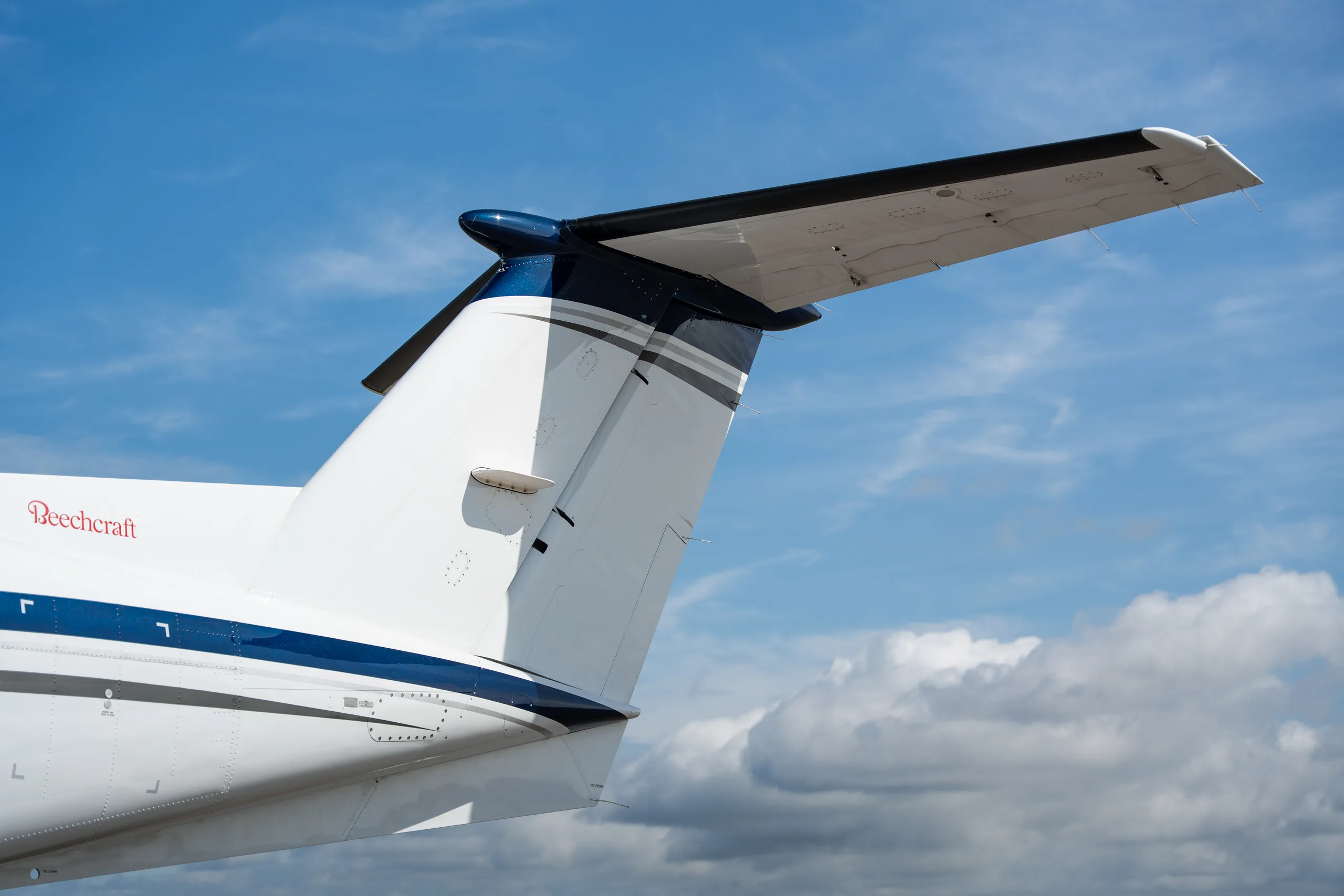 A close-up view of the white and blue T-tail of a Beechcraft King Air aircraft against a blue sky.