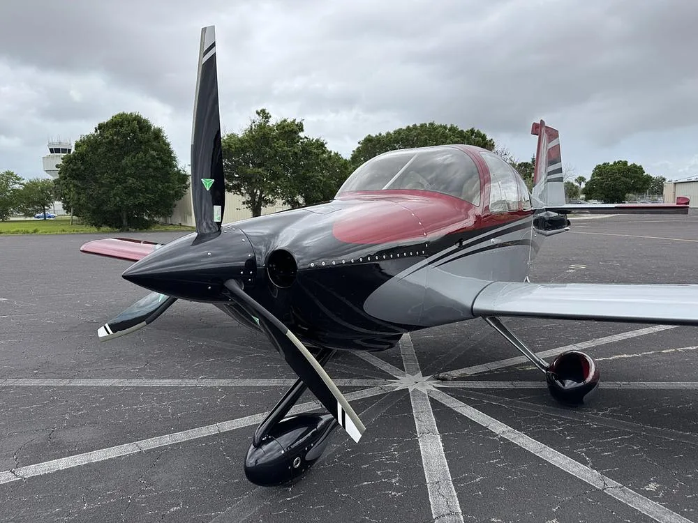 Front view of a red, silver, and black single-engine aircraft (N113KC) on an airport tarmac with an ATC tower in the background.