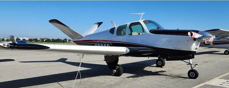 A white and black single-engine aircraft with red stripes, parked on an asphalt apron under a clear sky.