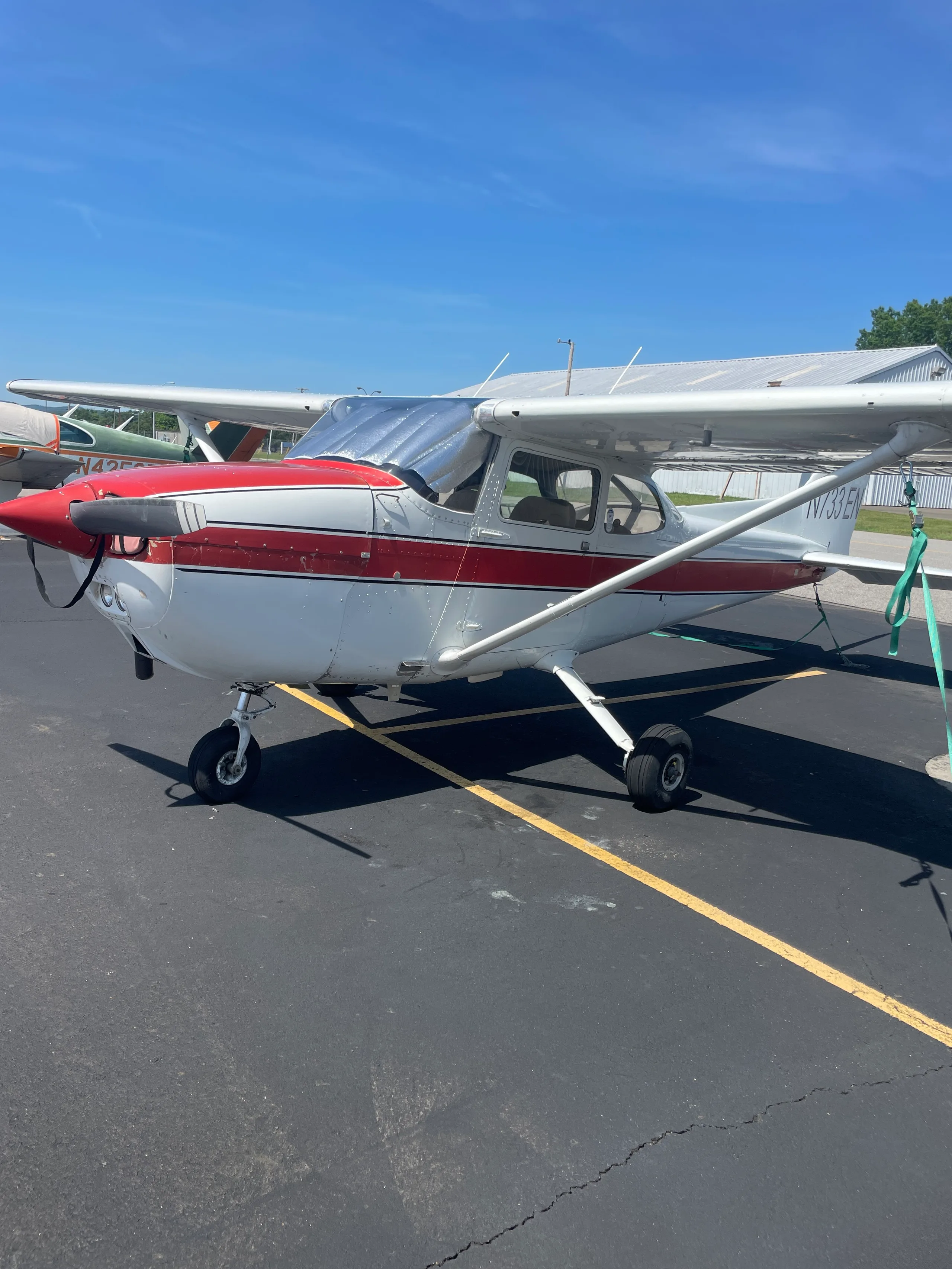 A white and red Cessna 172, registration N733EN, parked on an asphalt ramp on a sunny day.
