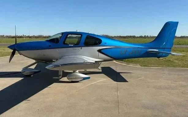 A blue and silver Cirrus SR22 aircraft, registration LV-JYU, parked on an airfield tarmac.