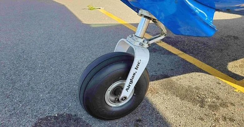 A close-up view of the nose landing gear and tire of the aircraft, with "Airglas, Inc." visible on the strut.