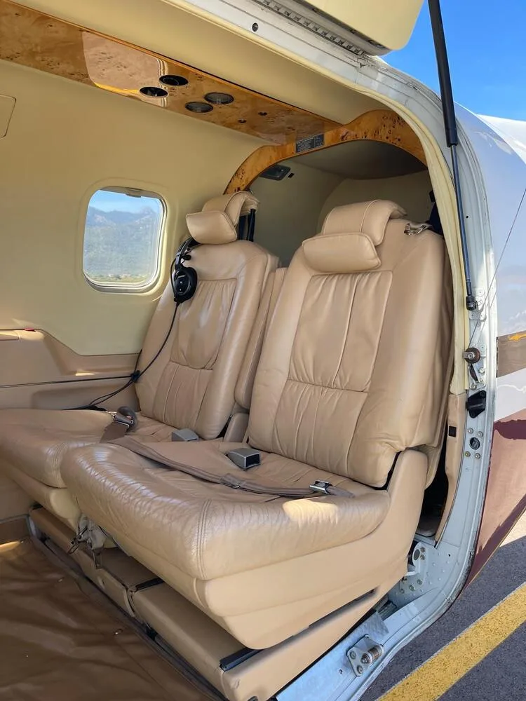 The tan leather interior cabin of an aircraft, viewed through the open passenger door, showing two rows of seats.