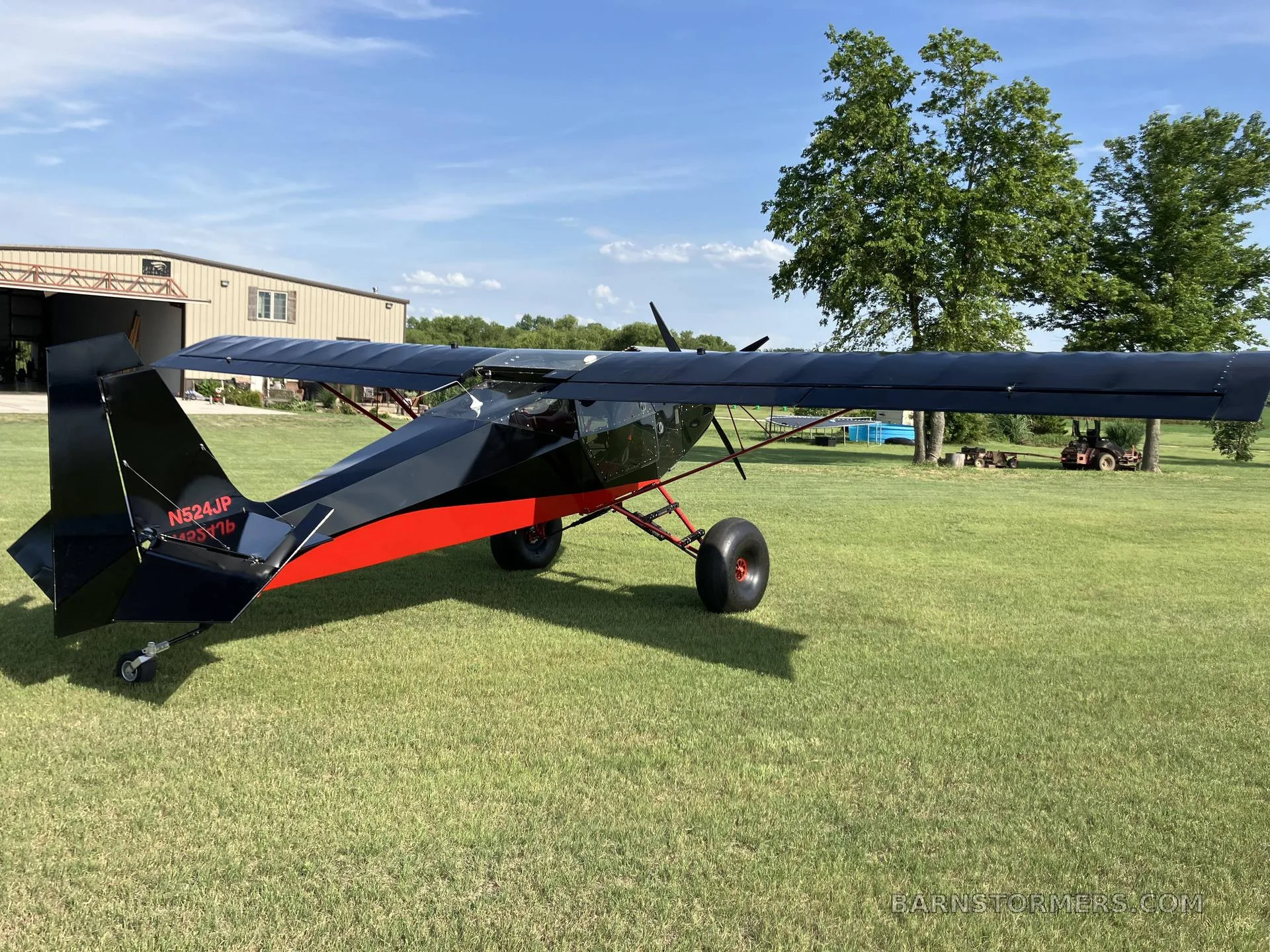 The rear-left view of a black and red bush plane with large tires parked on a grassy field.