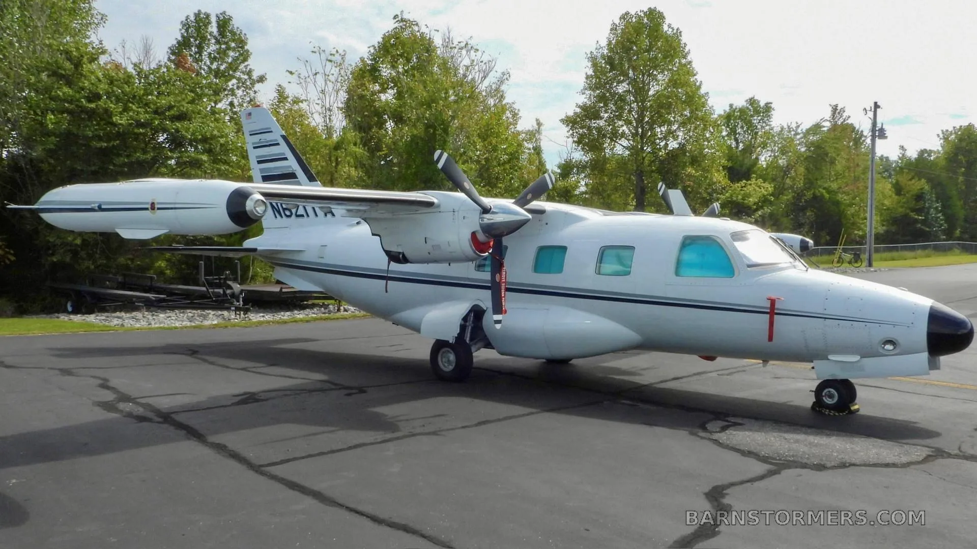 A white twin-engine turboprop aircraft, N621TA, with black accents, parked on an asphalt apron with trees in the background.