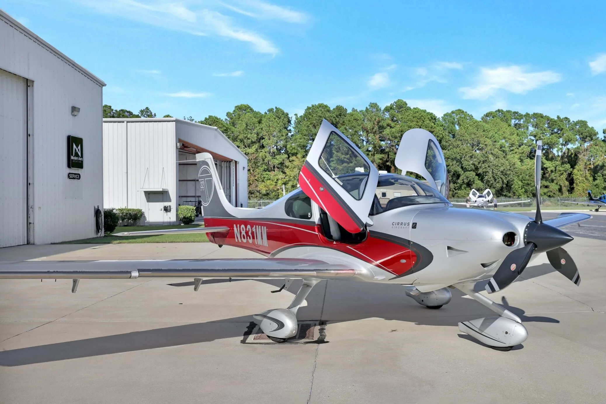 Front-side view of a Cirrus SR22T aircraft with red and silver paint scheme, registration N831MM, parked on an airfield with doors open.