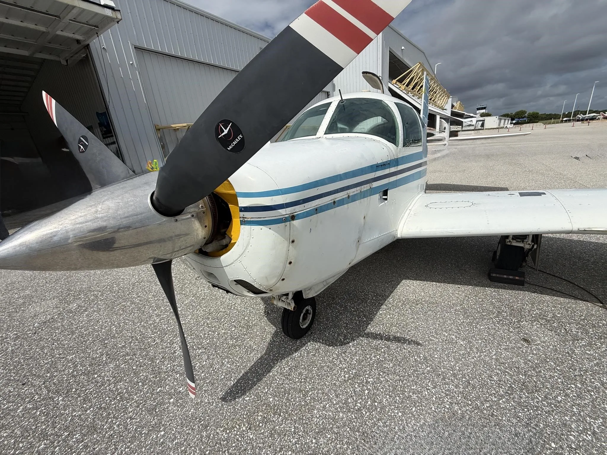 A close-up view of the front of the white single-engine aircraft N9234M, showing its propeller, engine cowling, and blue stripe details.