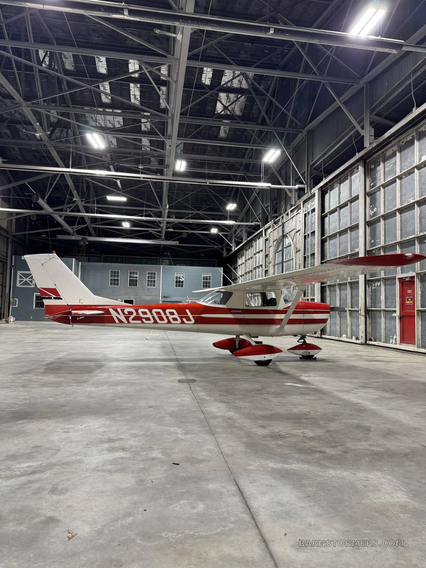 A red and white single-engine aircraft with registration N2908J parked inside a large hangar.
