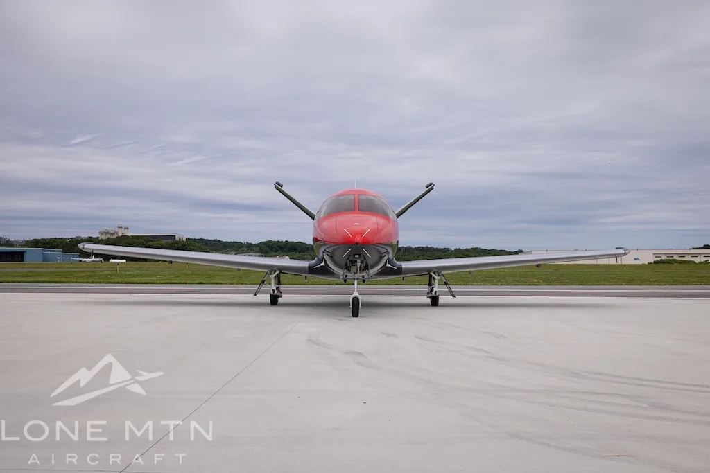 A head-on view of the Cirrus Vision Jet N204HS in red and grey, parked on an airfield.