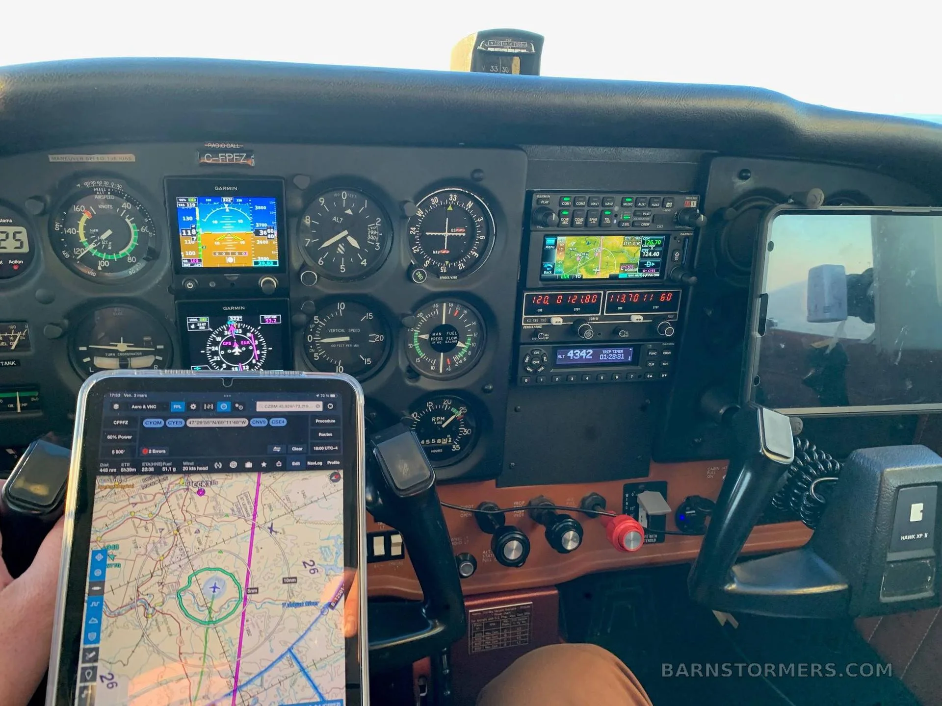 The cockpit of an aircraft, showing the instrument panel with analog gauges and modern digital displays, with a tablet displaying a map in the foreground.