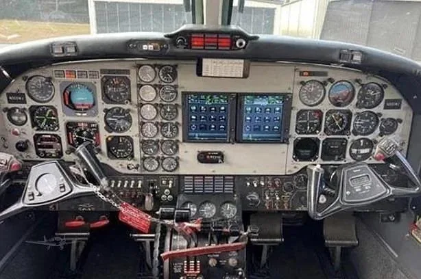 View of an aircraft cockpit with a complex instrument panel featuring analog gauges and two modern digital displays.
